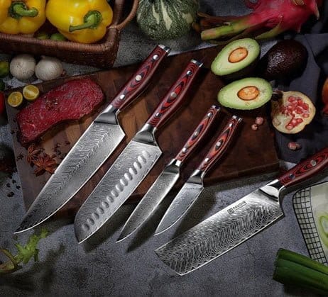 A set of five chef's knives with patterned blades and wooden handles displayed on a kitchen counter surrounded by assorted fresh vegetables and fruits.